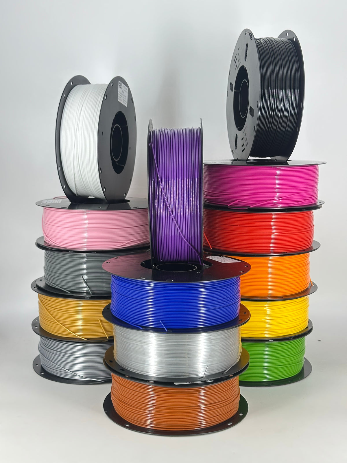 Stack of OzFDM PETG Basic spools in white, black, grey, purple, pink, red, yellow, orange and silver